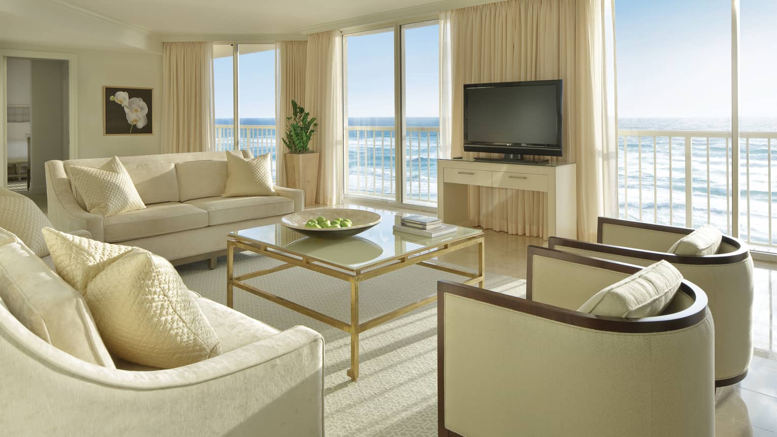 Deluxe Oceanfront Suite with white sofas and armchairs, glass coffee table, juliet balcony, ocean view
