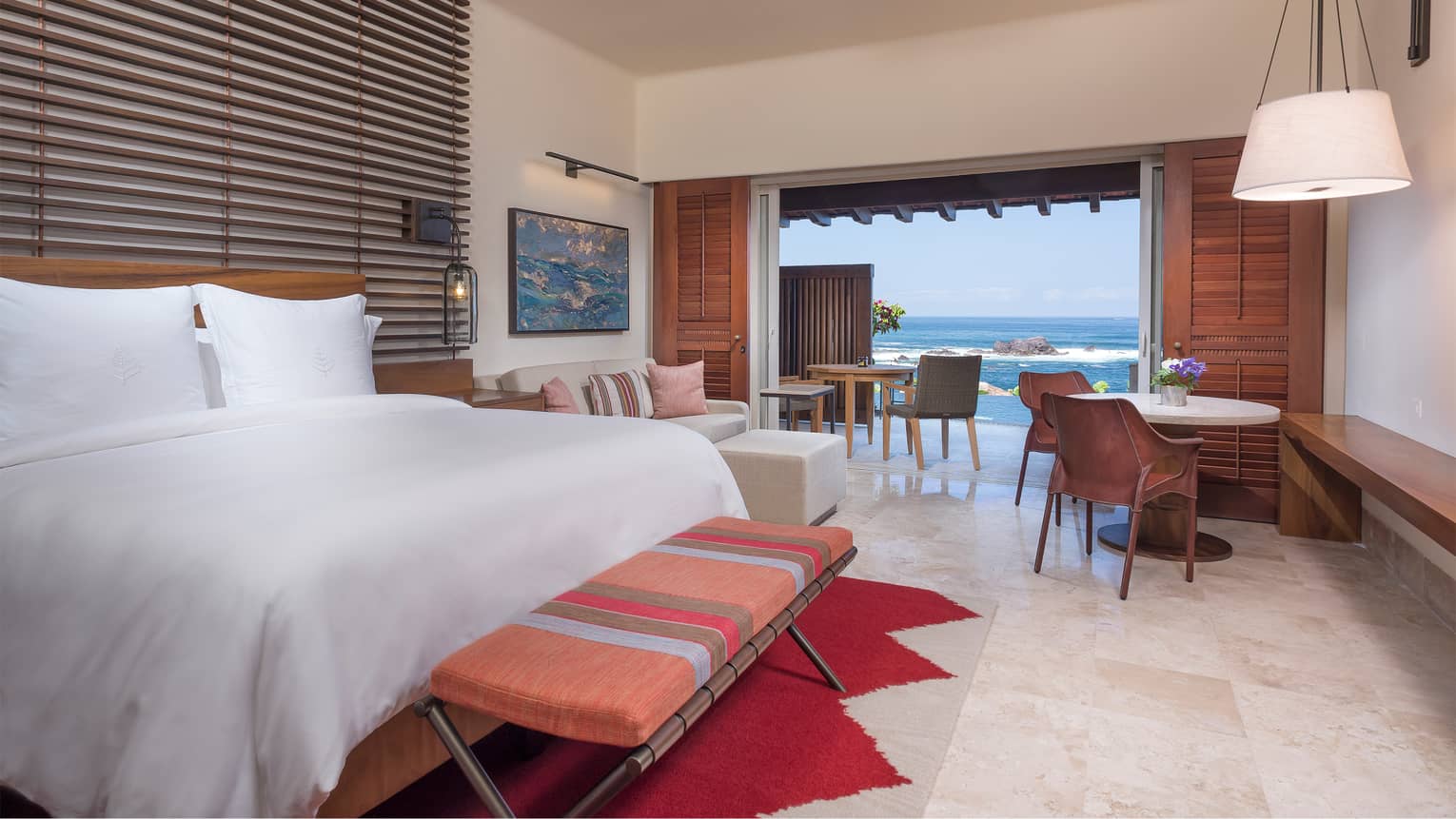 Sol Suite with white tile floors, bed, bench, loveseat, cafe table, sliding doors to patio with ocean view