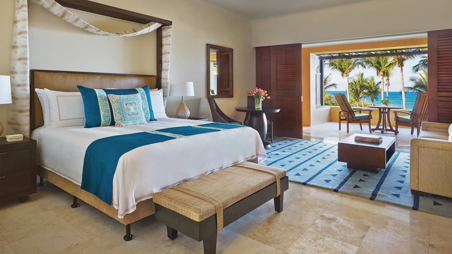 Casita room ocean view bed with blue spread and blue-and-yellow pillows, living area and open doors to covered patio