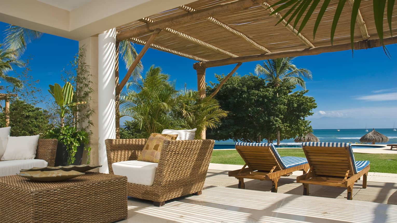 Sunny private beachfront residence patio with wicker furniture, bamboo awning, ocean view