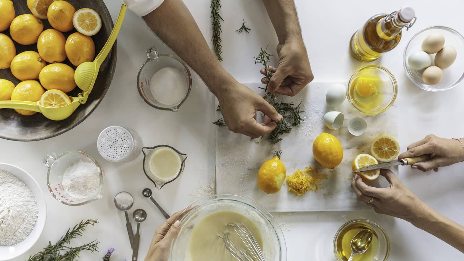 Aerial view of counter with people mixing batter in bowl, cutting fresh lemons and Thyme