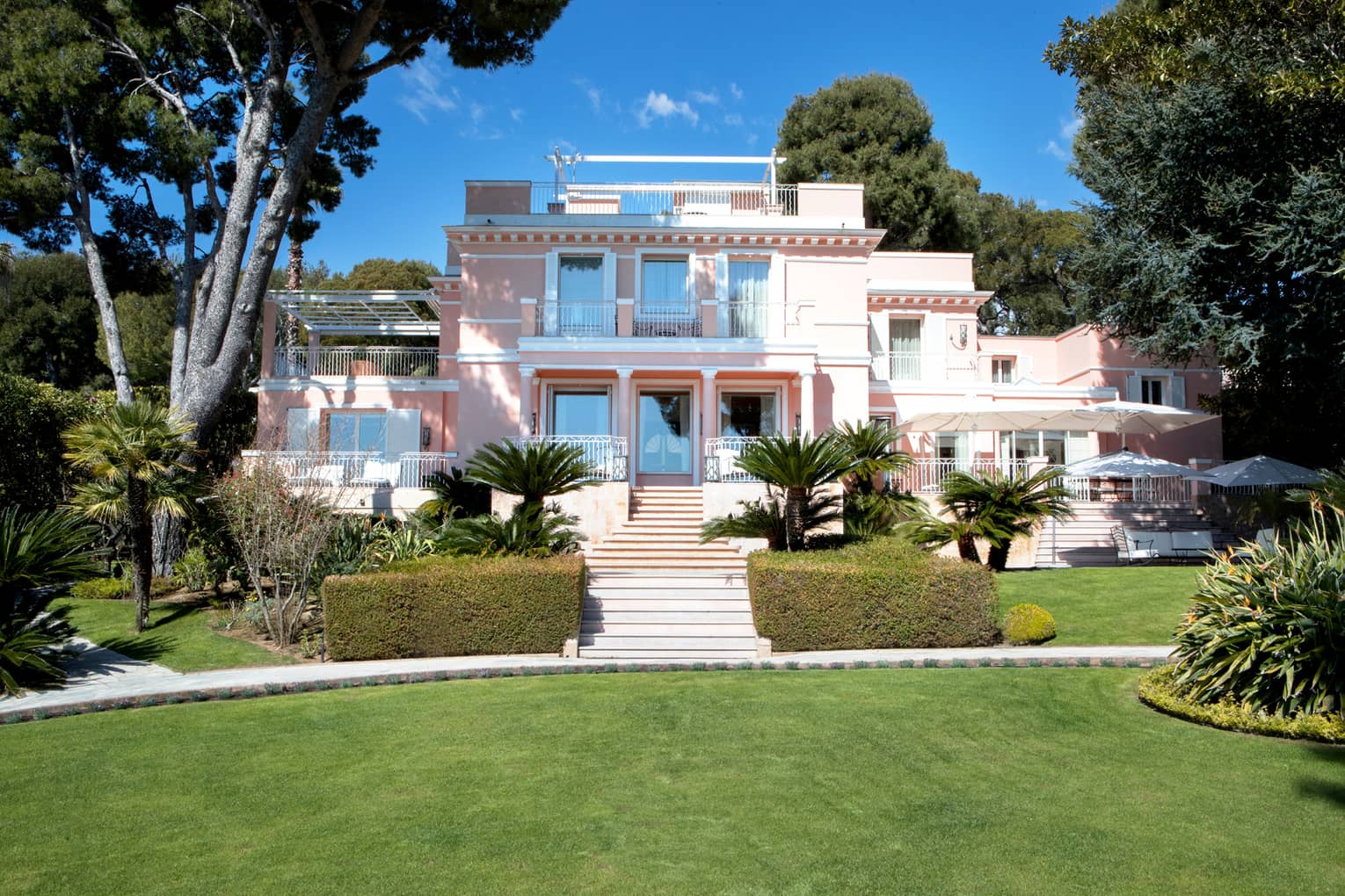 Manicured gardens, steps up to large three-storey pink villa
