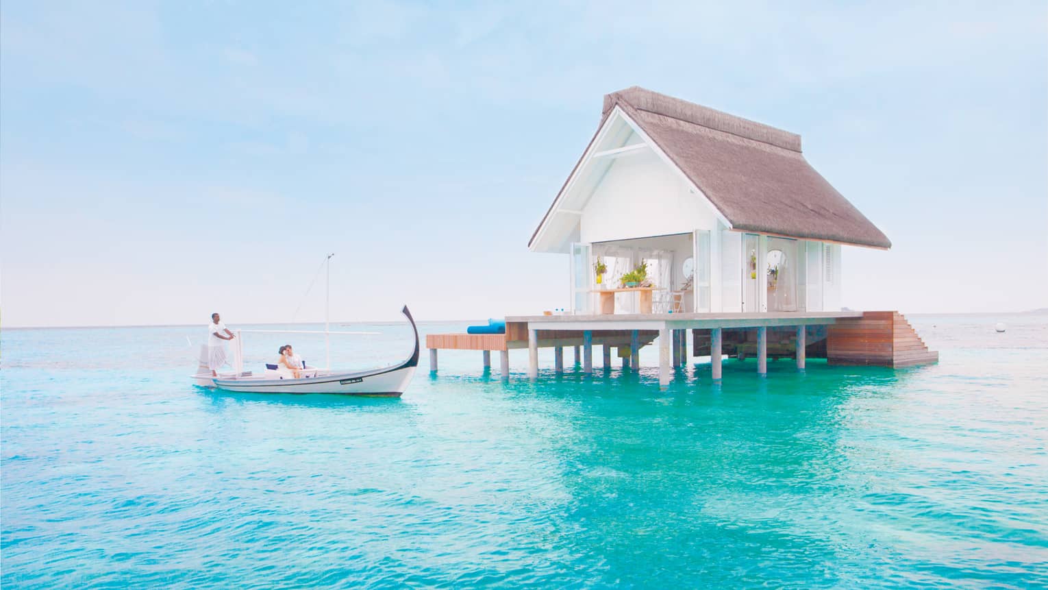 Bride and groom in white canoe on blue lagoon under small white bungalow 