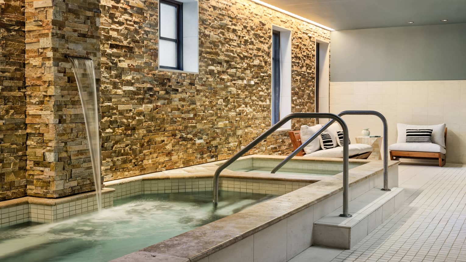 In-ground whirlpool area with waterfall, stone wall and cream sofas