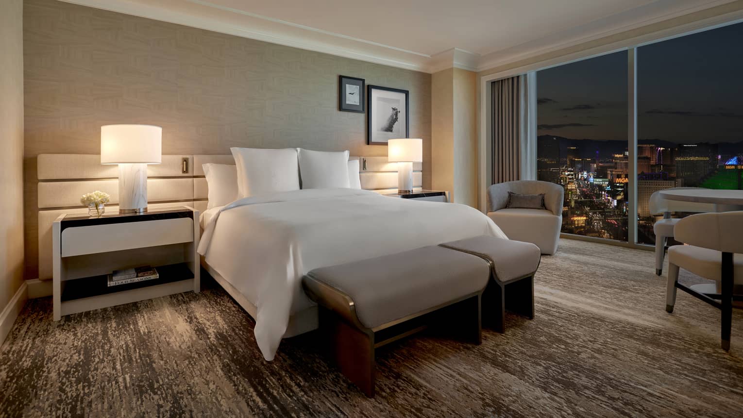A dimly lit room with bed, large window and two side tables.