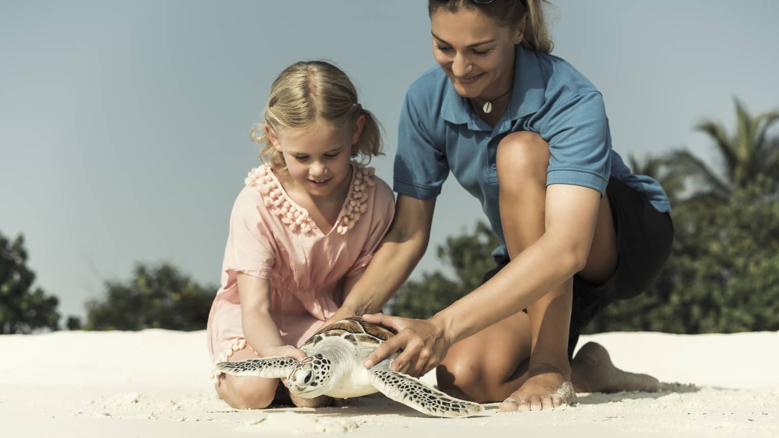 Hotel staff, young girl hold sea turtle over white sand beach