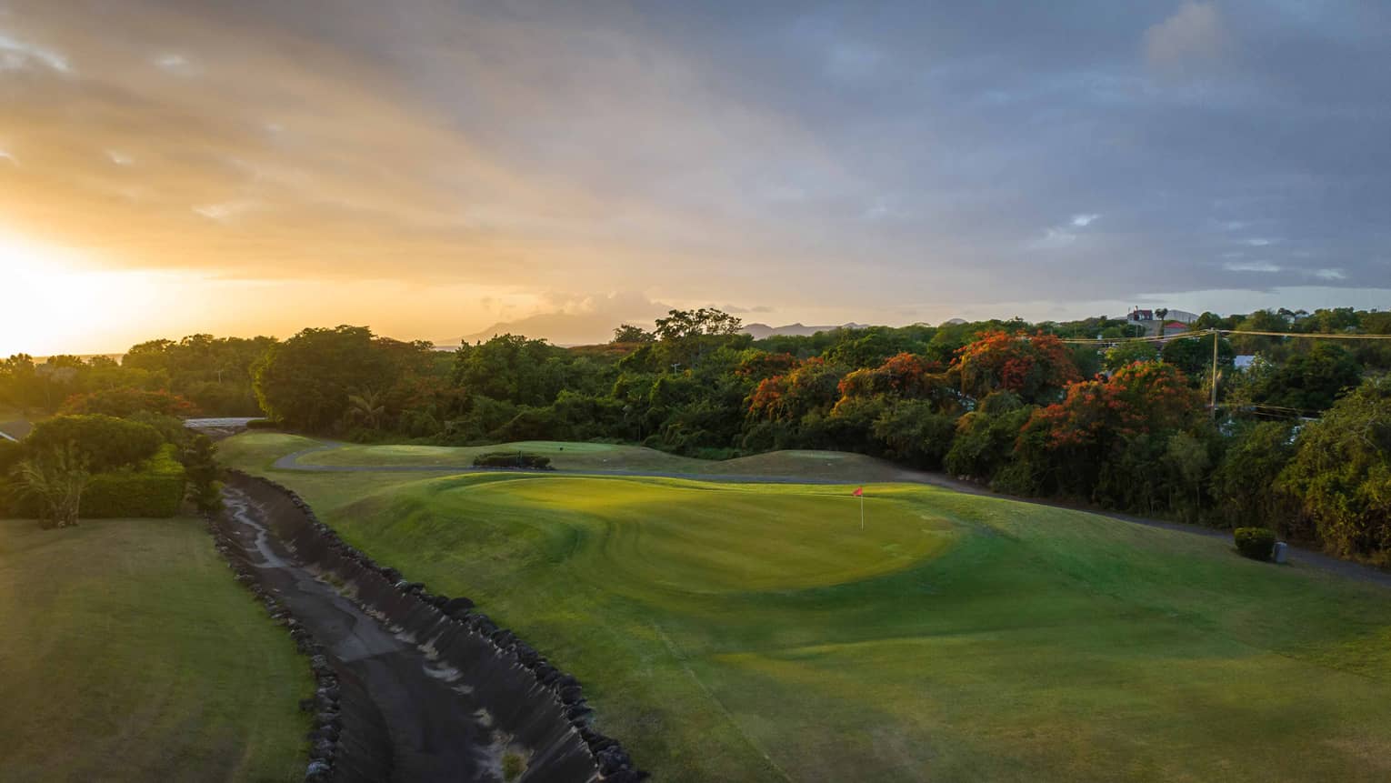 Dramatic sunset over a bright green golf course surrounded by trees and lush vegetation