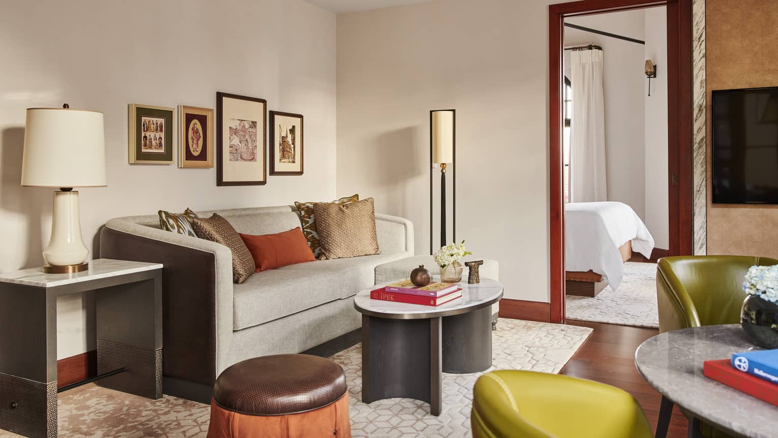 Hotel suite living room with beige couch and pictures on wall behind and oval coffee table on rug