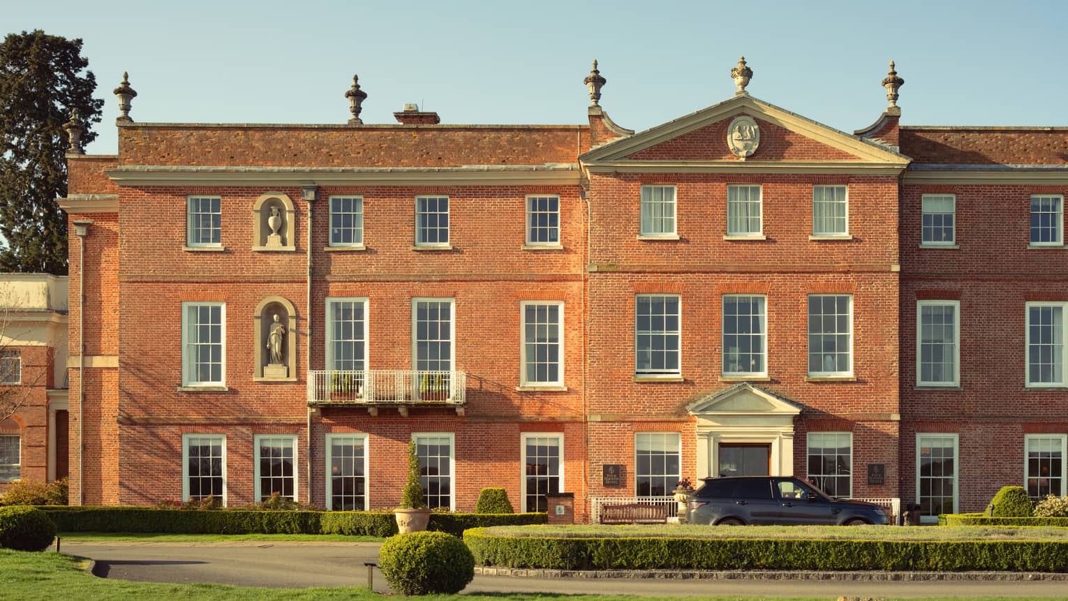 Stately red building with luxury SUV parked in front and expansive green lawn in forefront