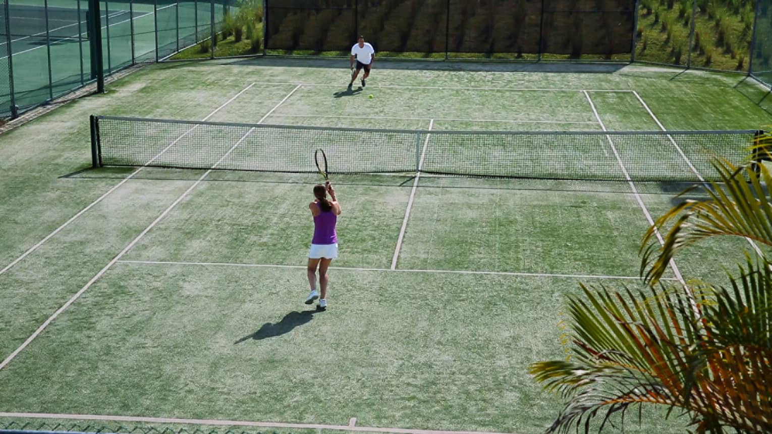 Aerial view of woman with tennis racket serving ball over net to man on court