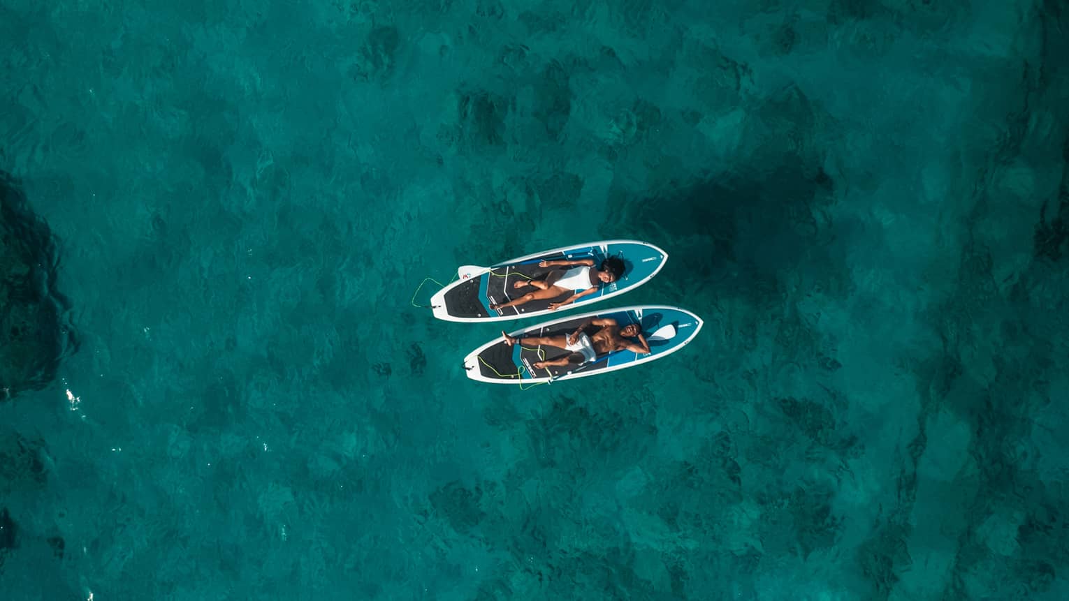 Two people lay on SUP paddleboards on the water