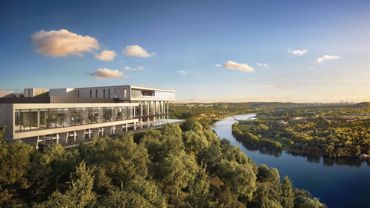 Modern building overlooks a river with a city skyline in the distance, amid lush greenery and a serene sky.