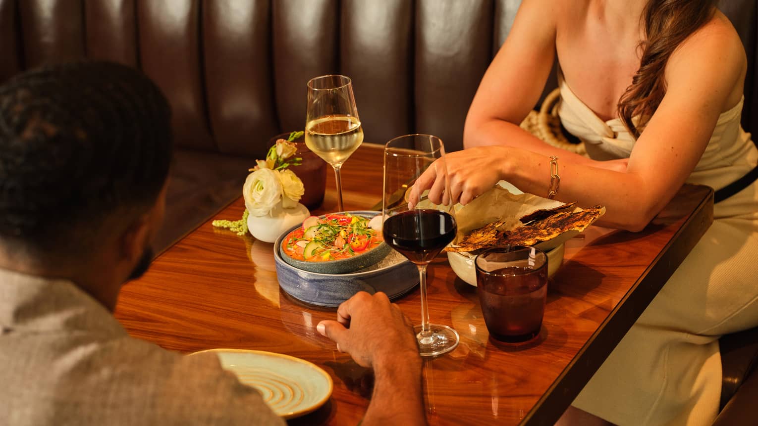 Two guests sitting at a dining table and eating a dish with wine glasses
