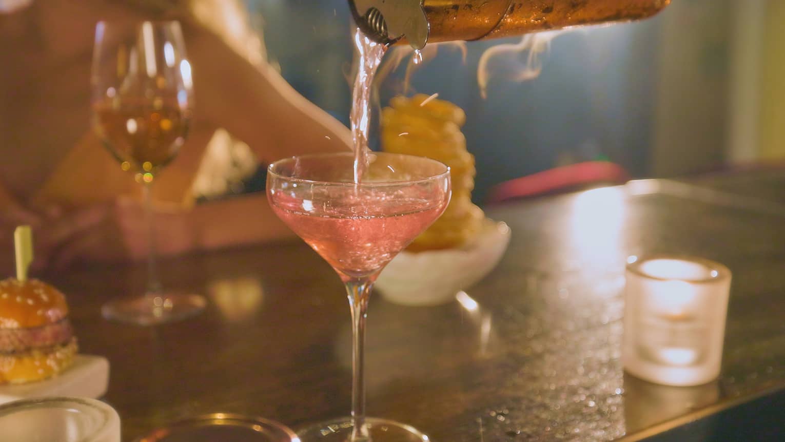Pink beverage being poured into a cocktail glass