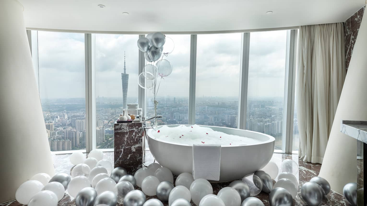Silver and white balloons surround free standing tub at window in Romance Room