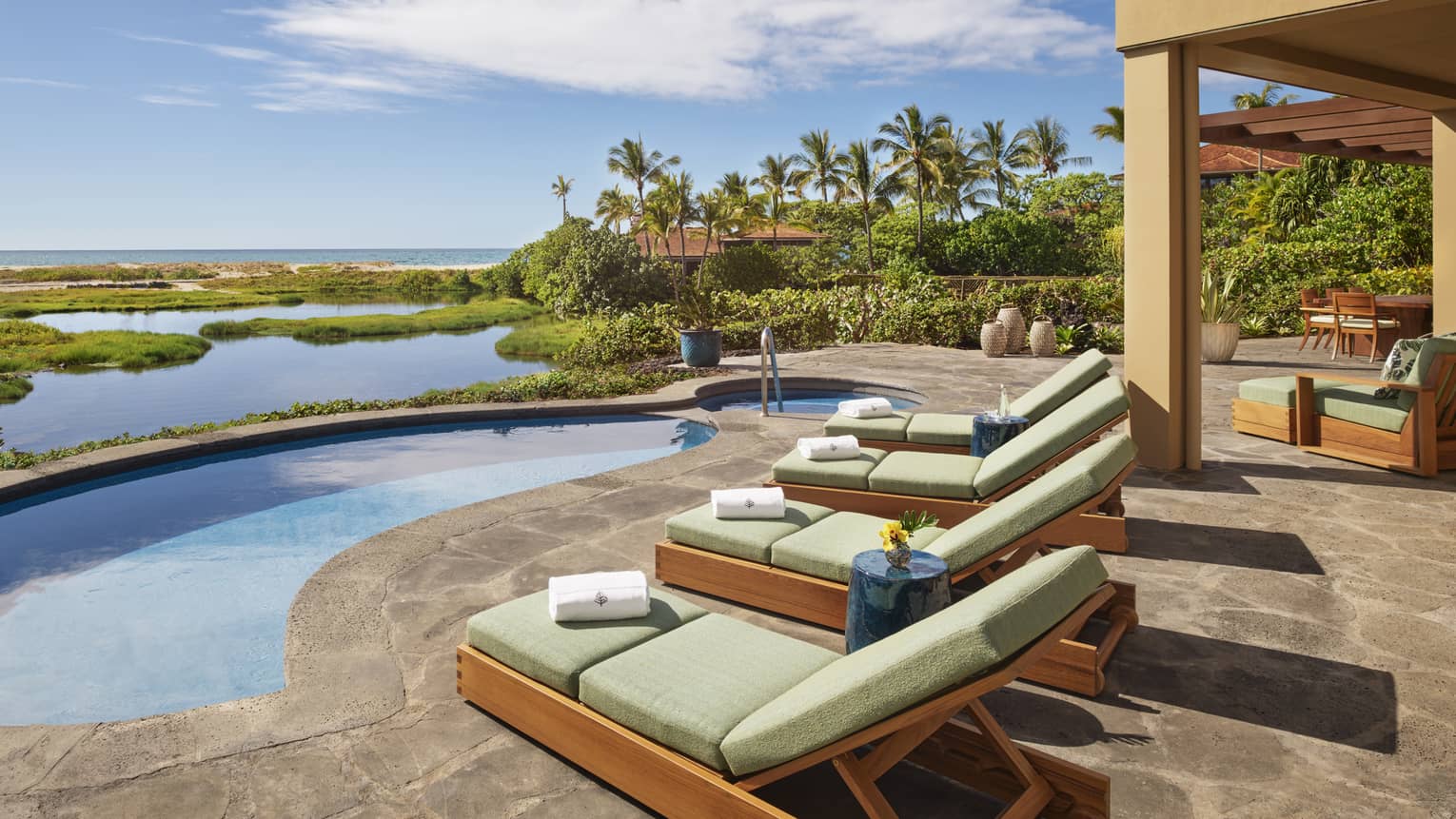 Beachfront patio with free form pool and four lounge chairs with light green cushions