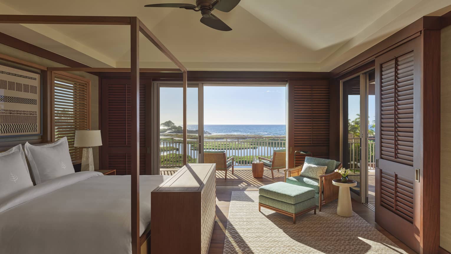 Bedroom with four-poster bed, green cushioned chair and ottoman, sea view