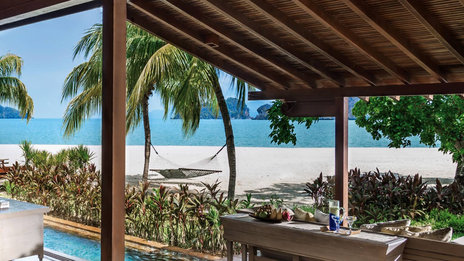 Villa awning over console table with fruit, drinks, plunge pool, by beach