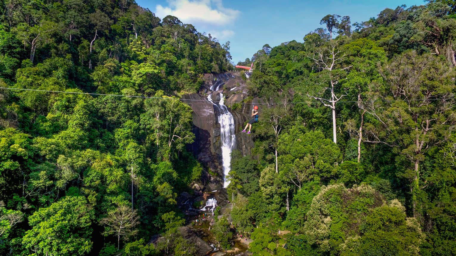 A four seasons guest rides a zip line over a waterfall in Langkawi