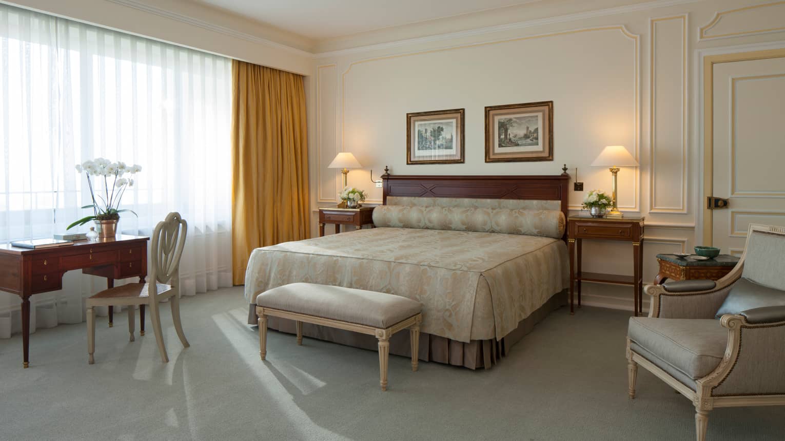 Royal Suite bed with gold pattern linens, light velvet bench and armchair, desk, sunny window with closed curtains