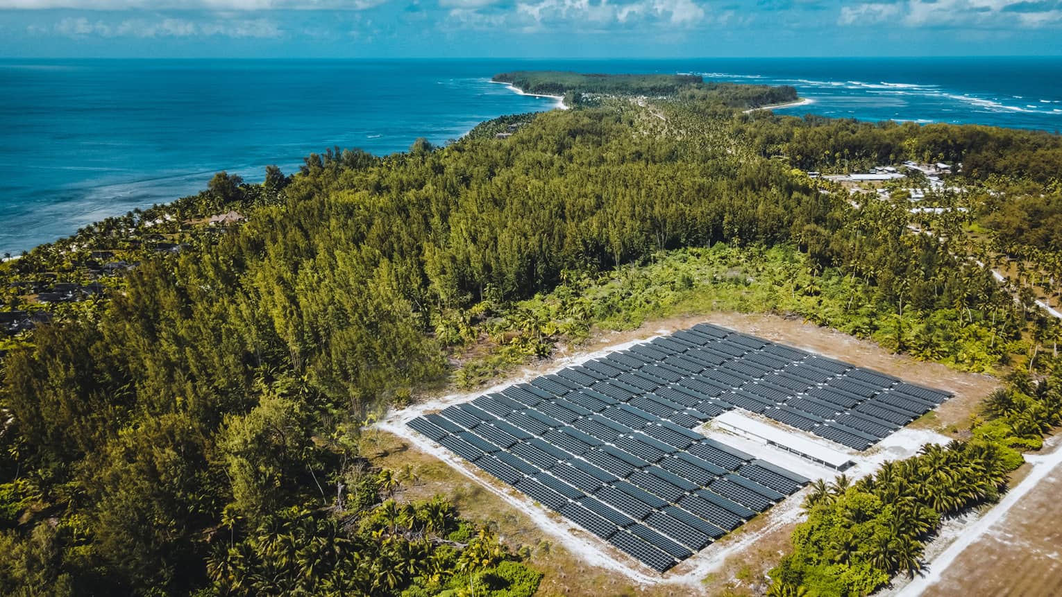 The Solar Farm at FS Seychelles Desroches, rows of panels surrounded by greenery and the Indian Ocean