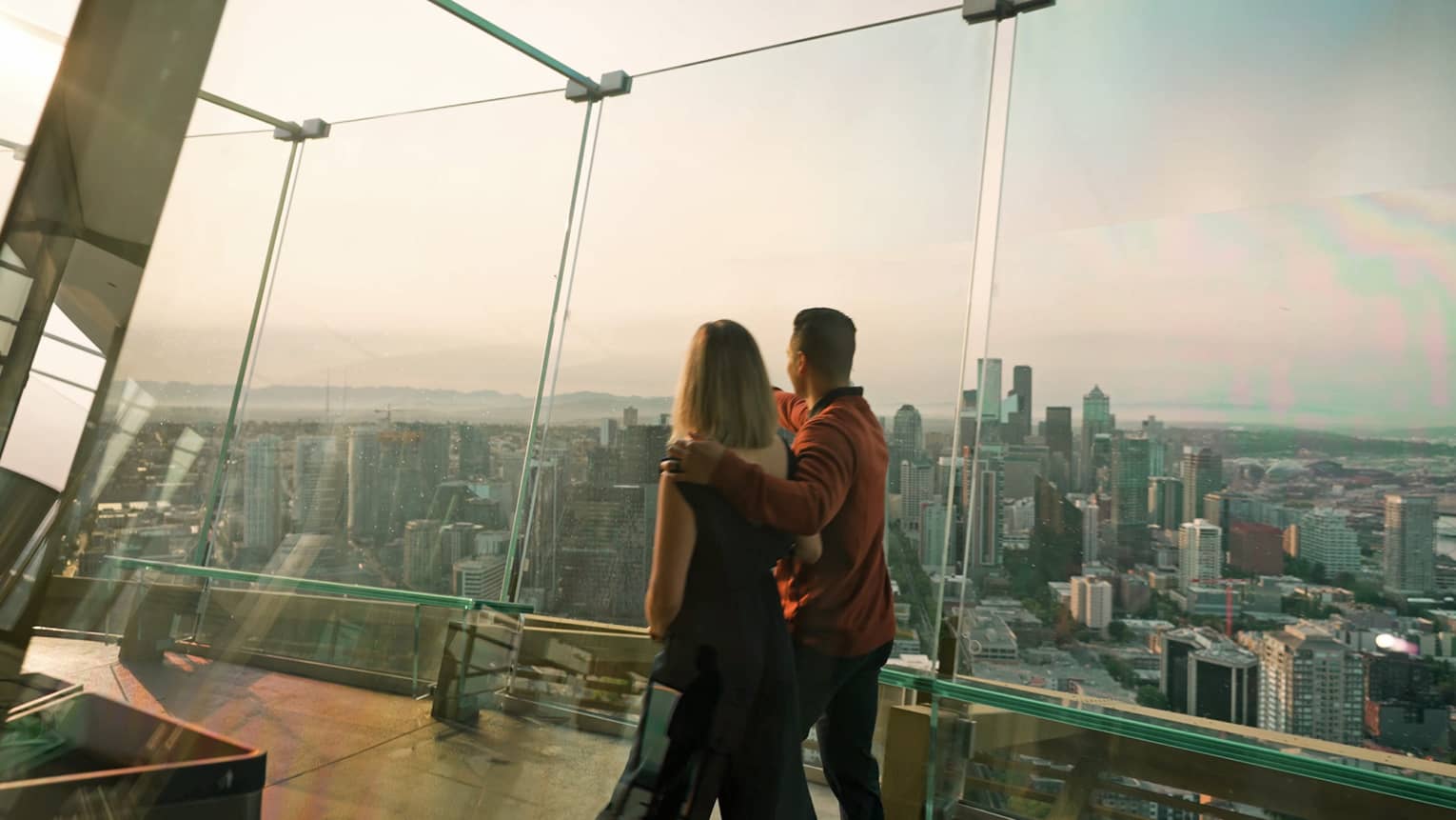 A man and woman walking in a tall building with glass walls looking out at a city.