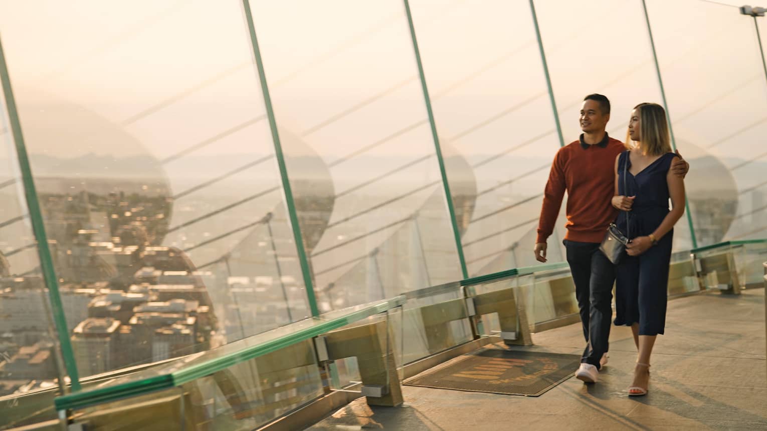 A man and woman walking in a tall building with glass walls looking out at a city.