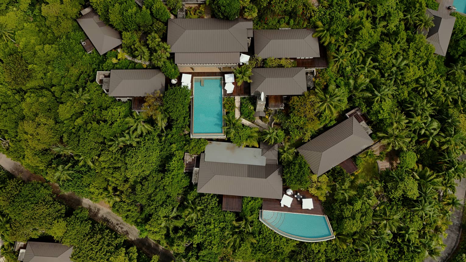 Aerial view of large eight-bedroom residence with two pools, nestled in jungle-like landscape