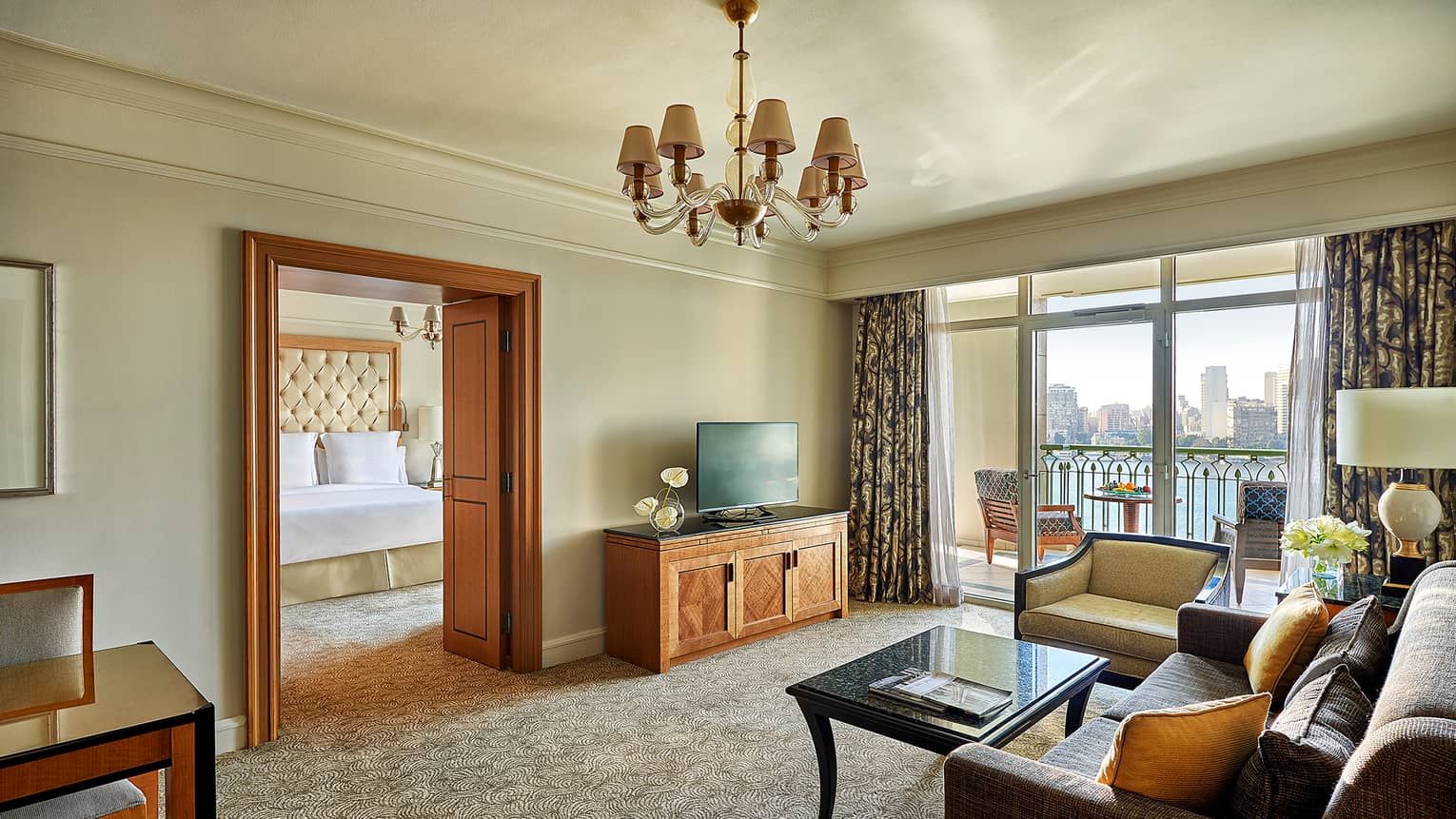 Suite living area with sofa, TV and coffee table, looking into adjoining bedroom at bed