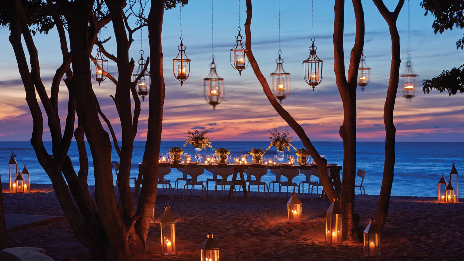 Lanterns hang from trees near dining table on Manzanillas Beach at sunset