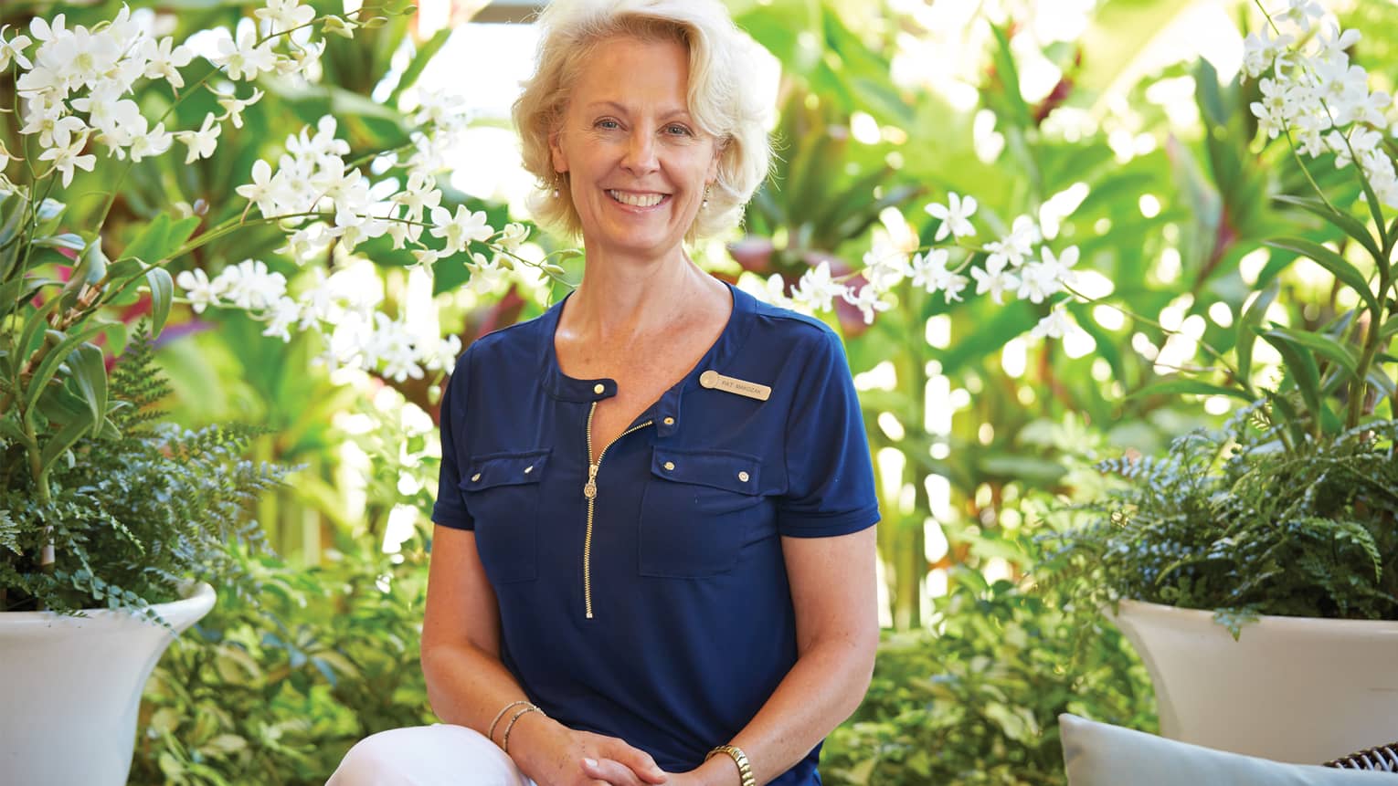 Portrait photo of Pat Makozak, Senior Spa Director between planters with tropical white flowers 
