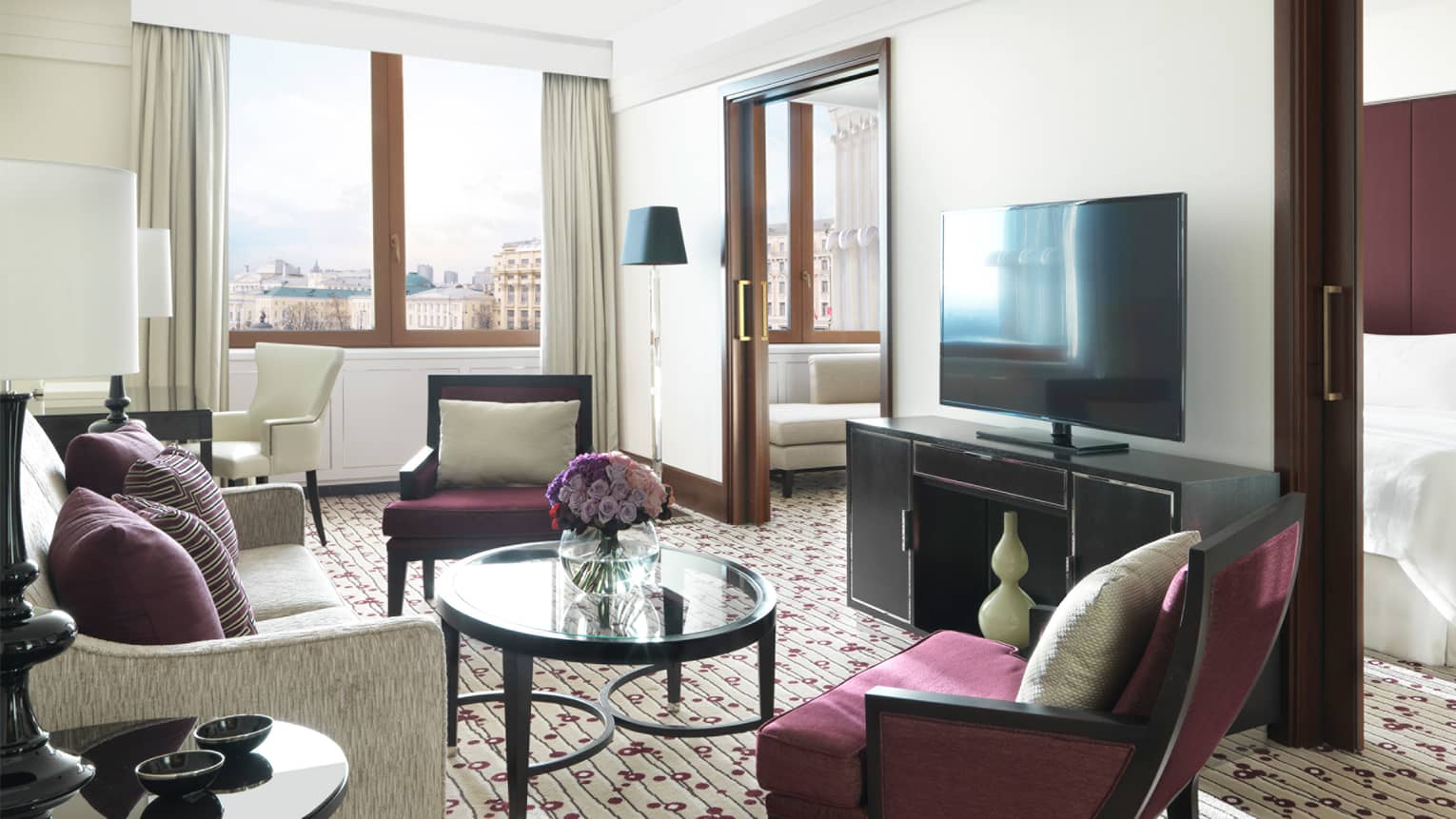 Executive Suite living area with burgundy accent chairs, flowers in glass vase, flat-screen TV on wall concealing bed