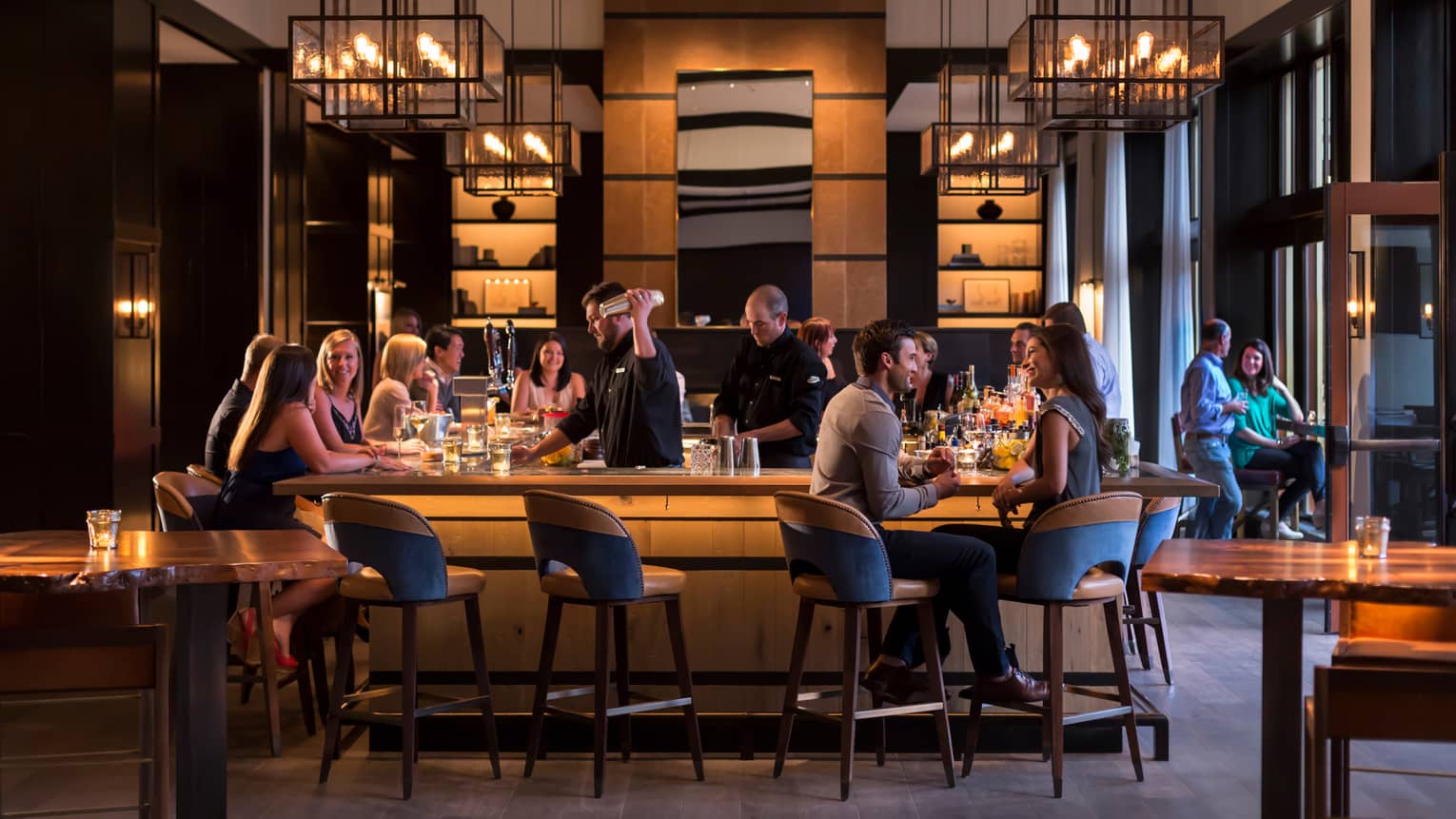 Vail Restaurants Fine Dining In Village Four Seasons Resort Guests Socialize Around Wood Bar With Mid Century Style Stools And Chandeliers As Bartender Makes