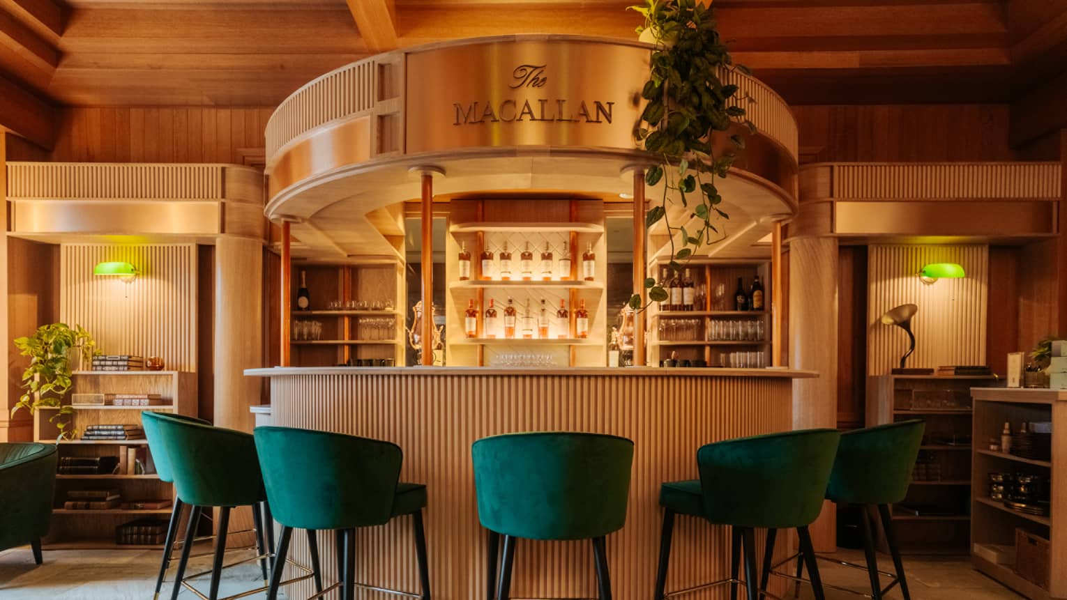 Half moon–shaped bar with green velvet bar stools and display of liquor bottles in background