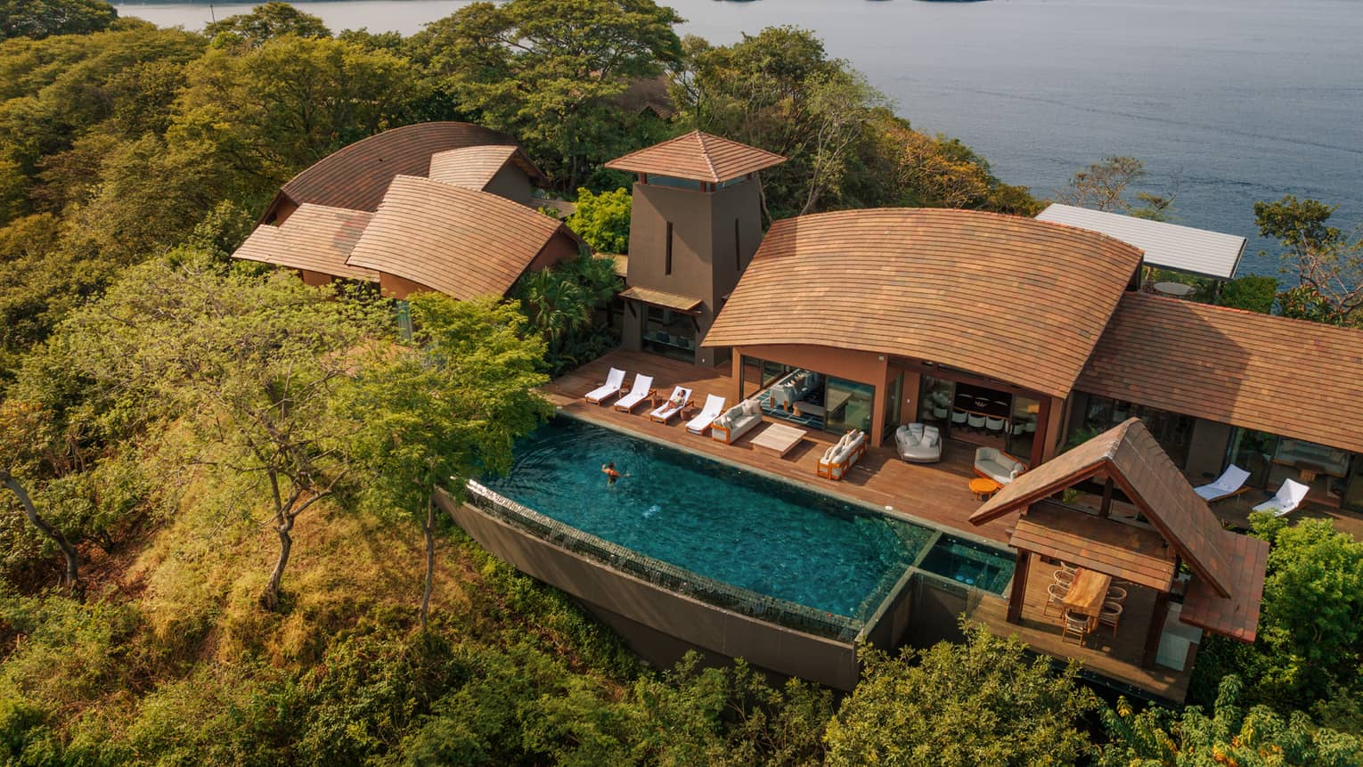Aerial view of private villa on a green hillside next to the ocean