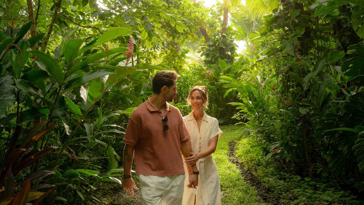 Couple walks hand in hand along a walkway surrounded by dense green tropical foliage