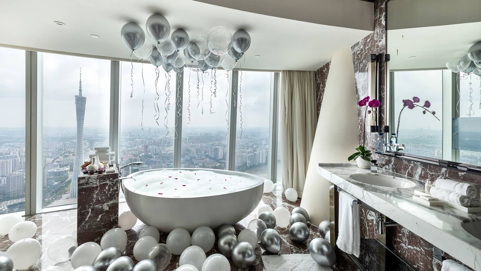 Silver and white balloons surround free standing tub at window in Romance Room