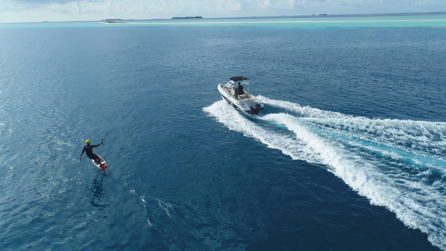 An aerial view of someone wakeboarding behind a small speed boat