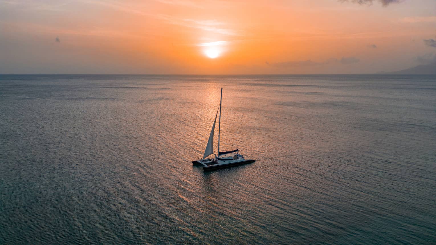 Aerial view of a sailboat floating through calm ocean waters at sunset