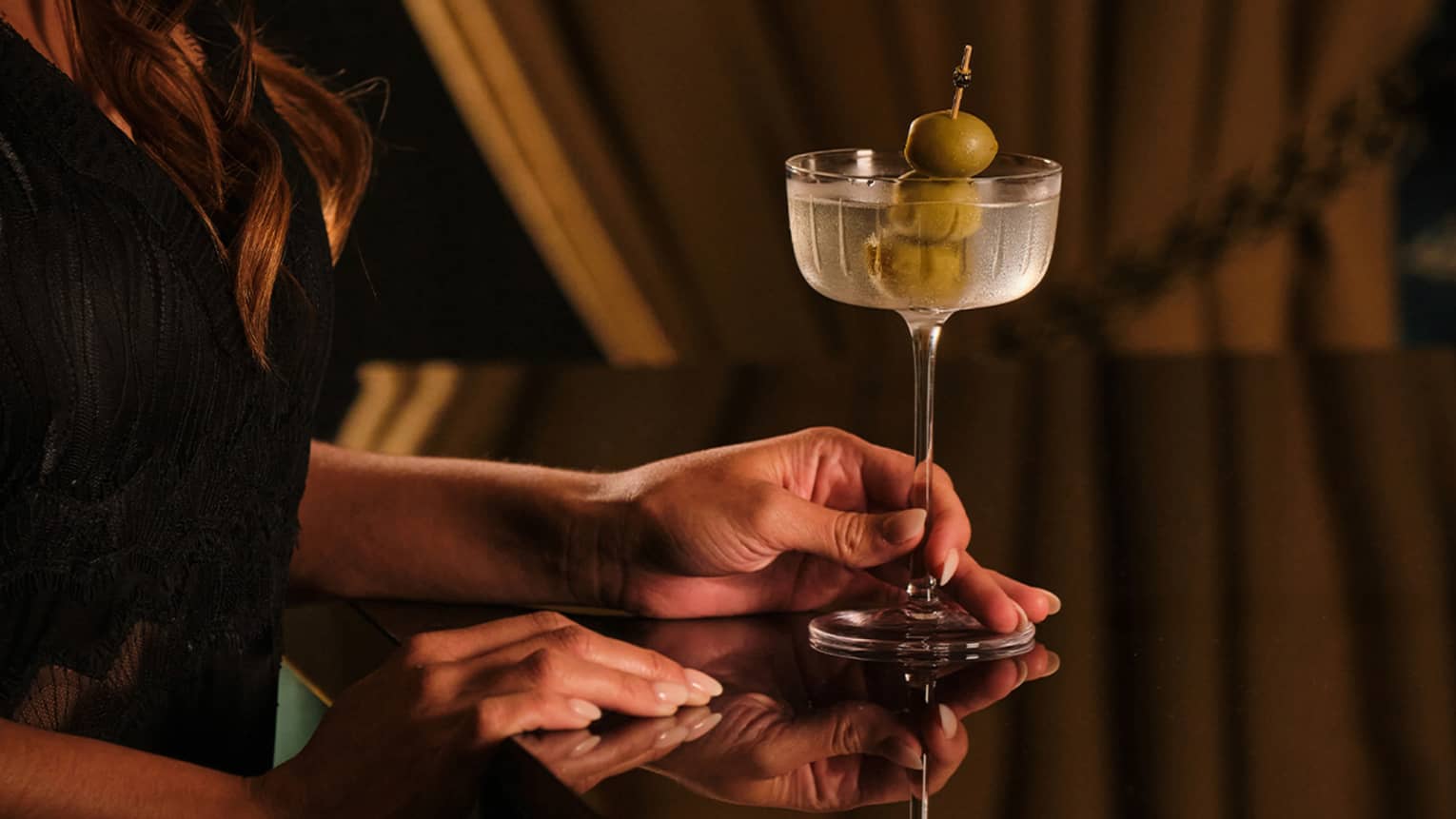 Person holding a drink glass with three olives in it.