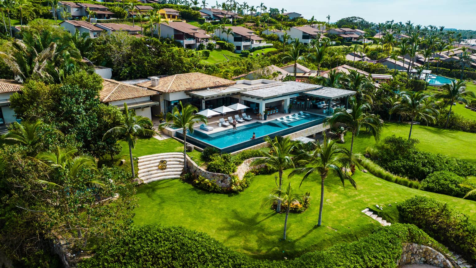 Luxury villa with large rectangular infinity pool and lush green landscaping by the ocean