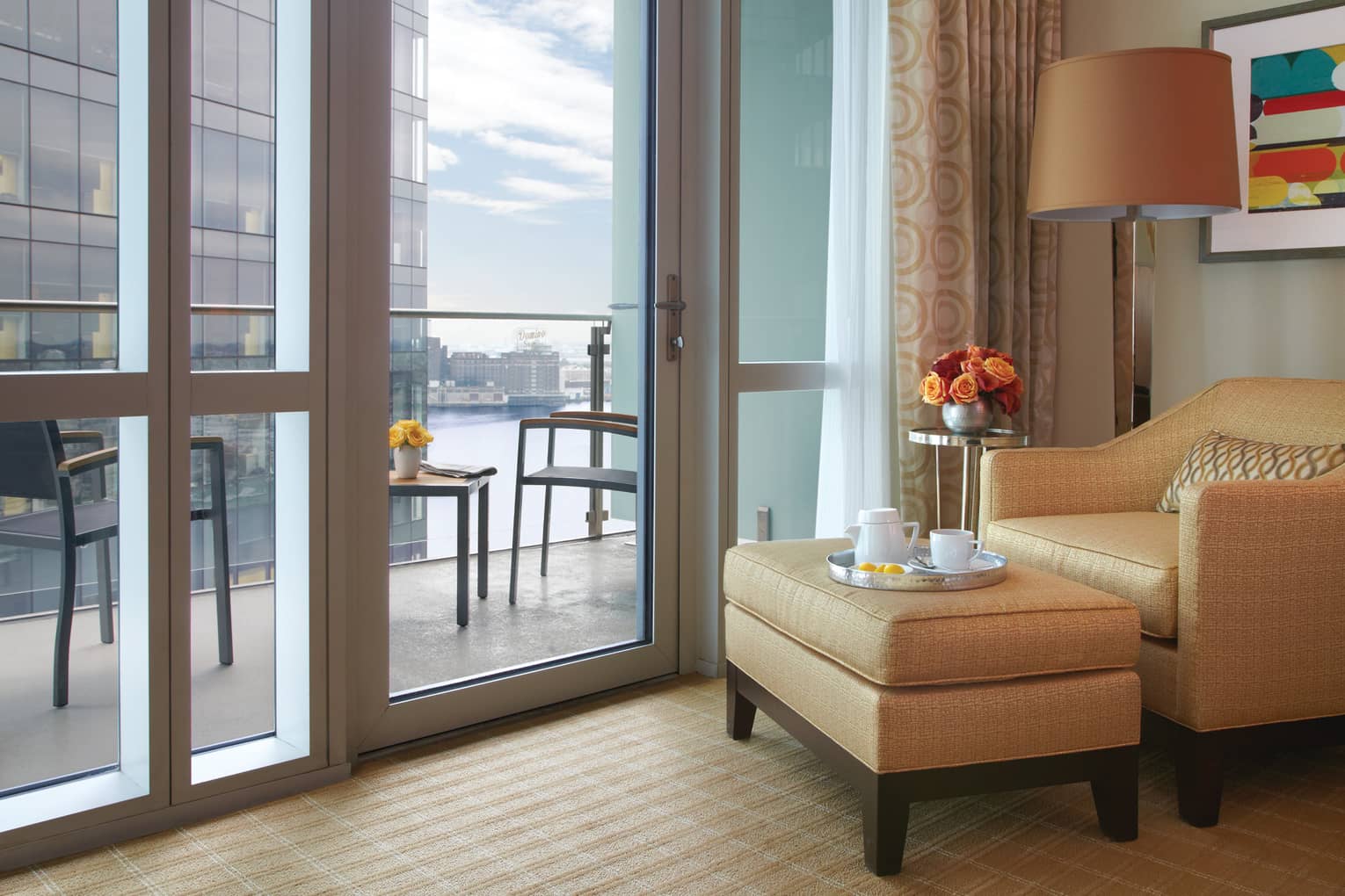 Harbour View Room gold armchair, ottoman with tea tray by glass wall, balcony door