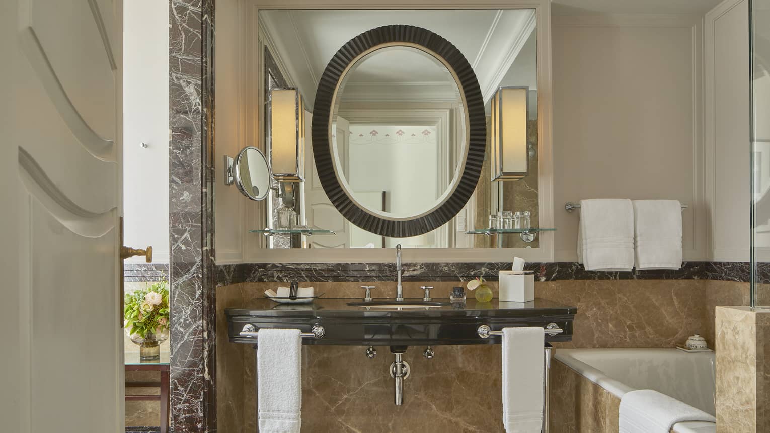 Bathroom with brown marble vanity, dark oval mirror and beige marble tub