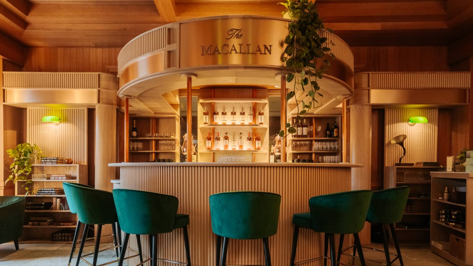 Half moon–shaped bar with green velvet bar stools and display of liquor bottles in background