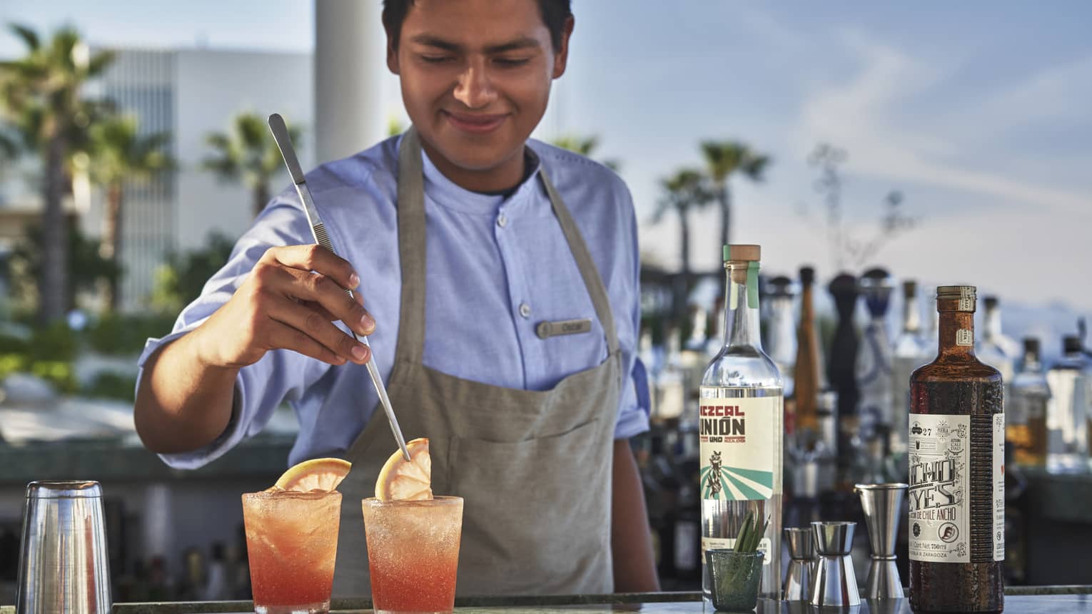 A Casa de Brasa mixologist garnishes two pink cocktails with a slice of citrus at an our door bar 