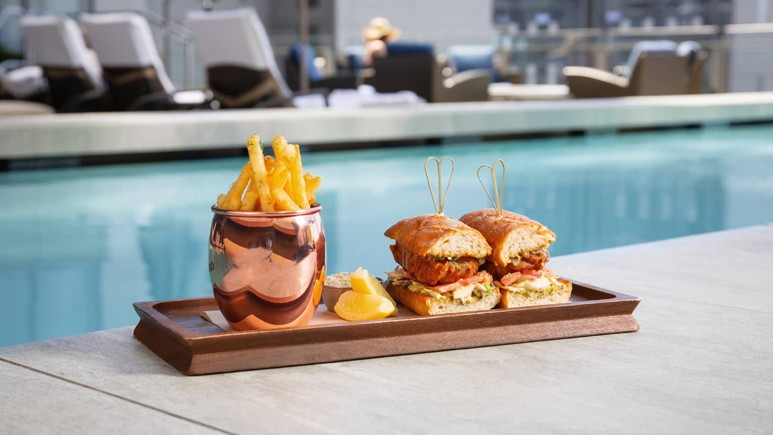 Crispy fish sandwich and fries on a tray next to a pool.