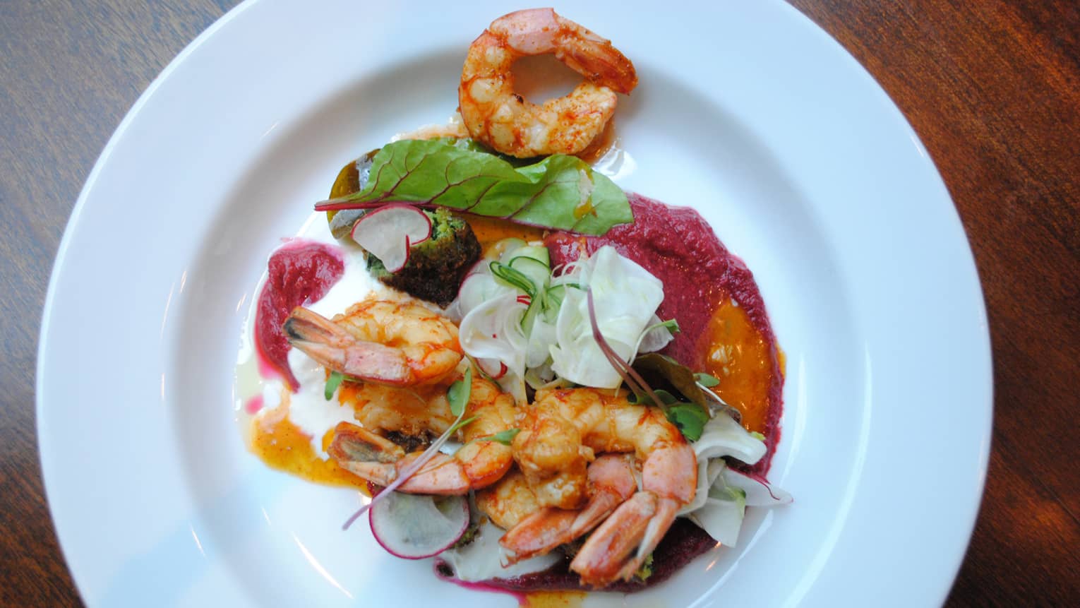 A shrimp dish is served with radishes, greens and a creamy sauce