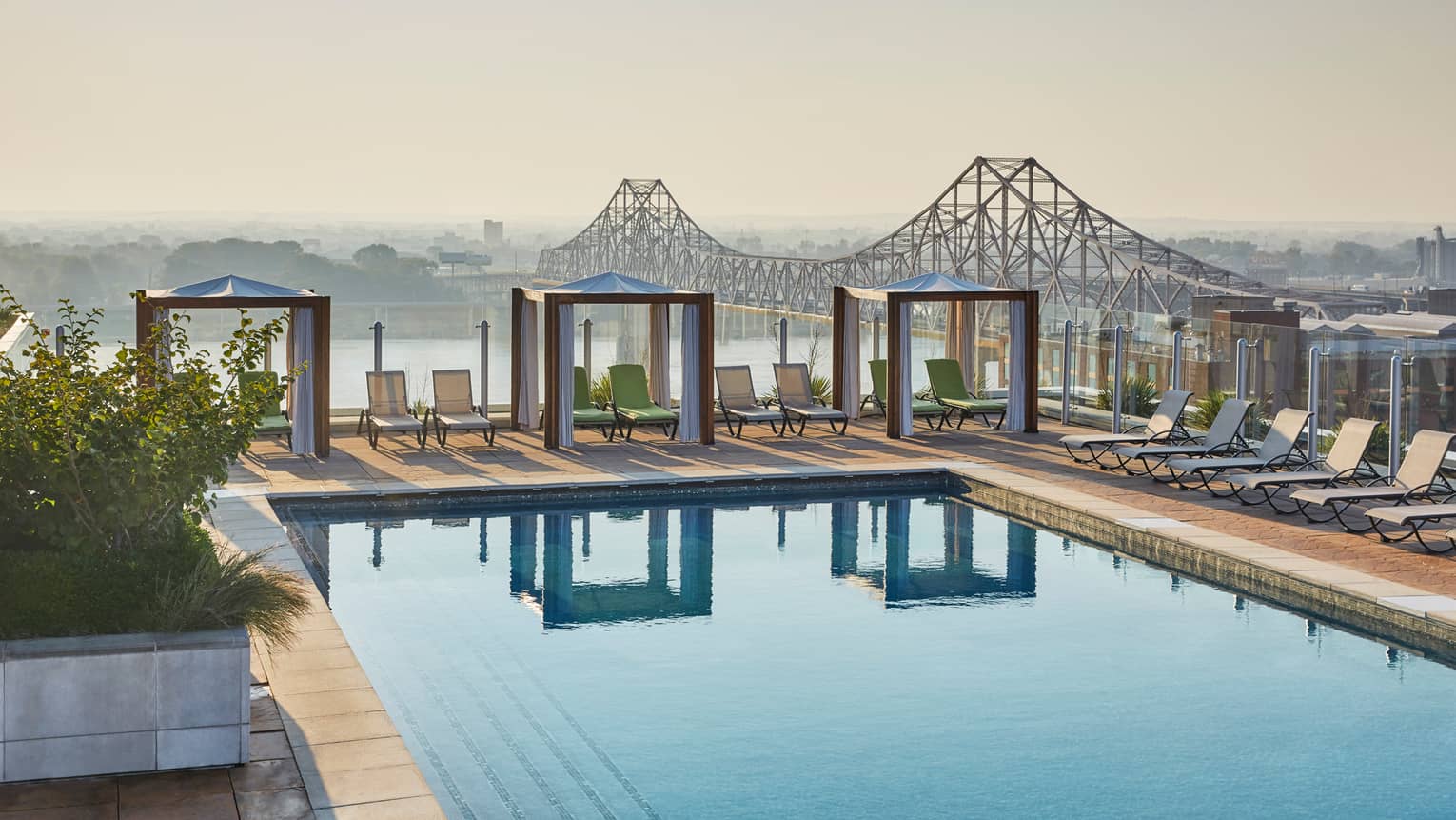 Rooftop swimming pool with three white cabanas, pool chairs, bridge and river in background
