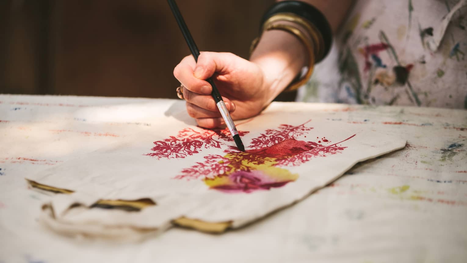 Close-up of woman with paint brushes painting flowers on canvas bag