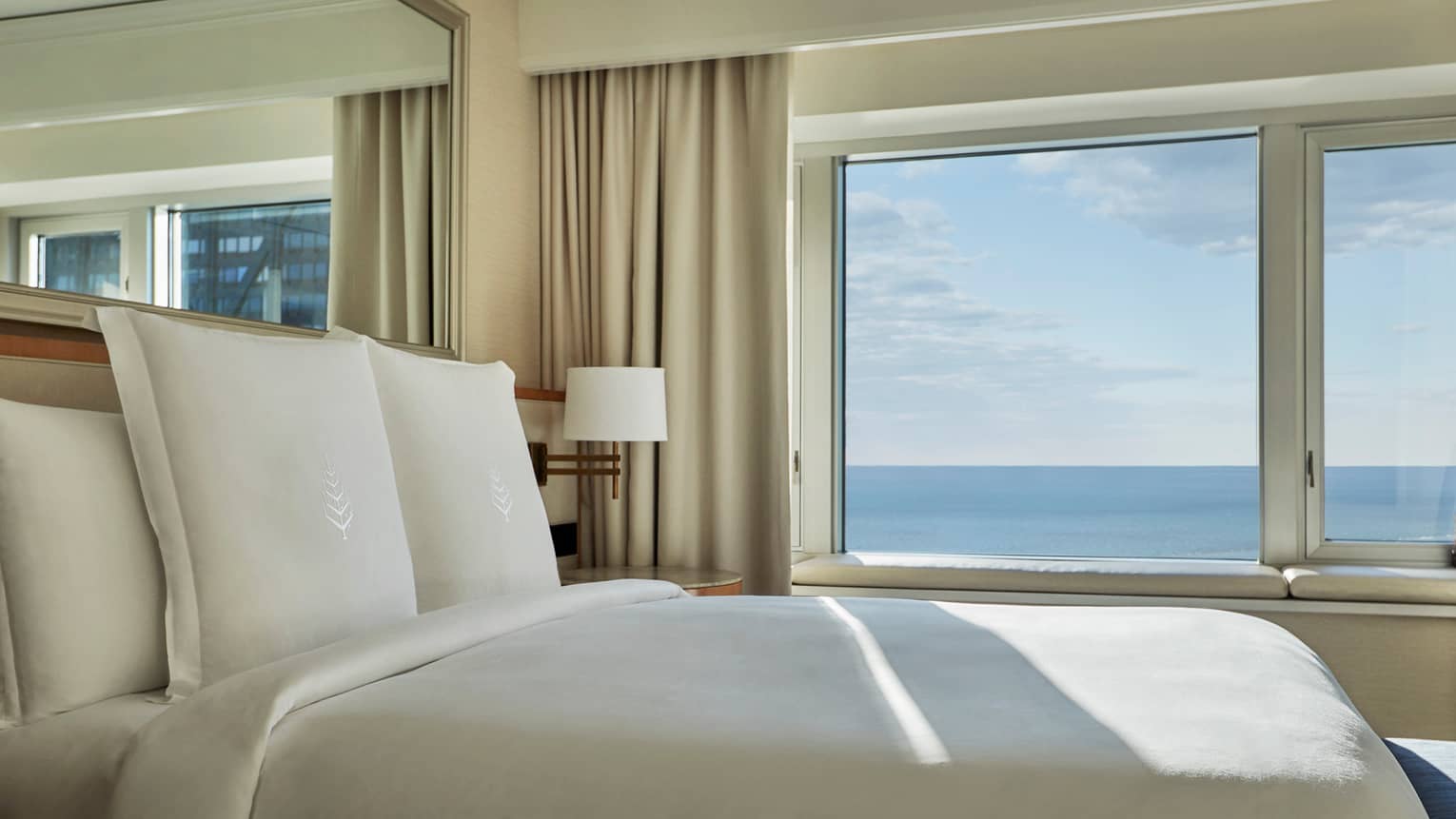 Close-up of hotel bed with white linens, Four Seasons logo by sunny window overlooking Lake Michigan